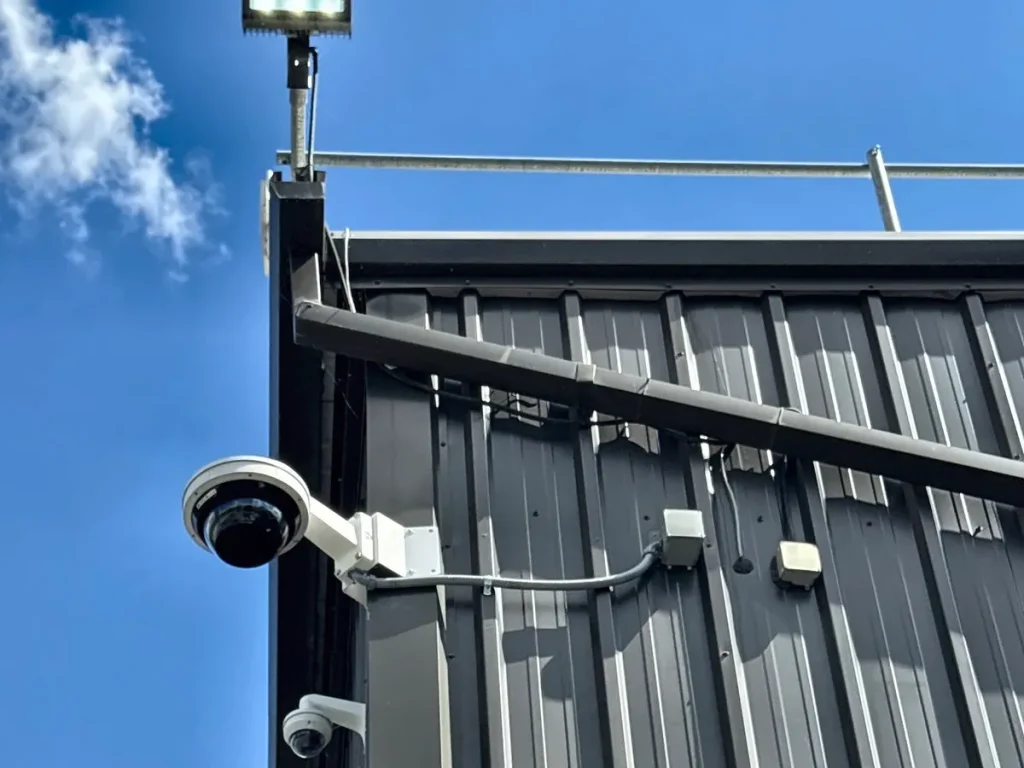 PTZ camera and a mini dome on the corner of a metal building, with a floodlight above